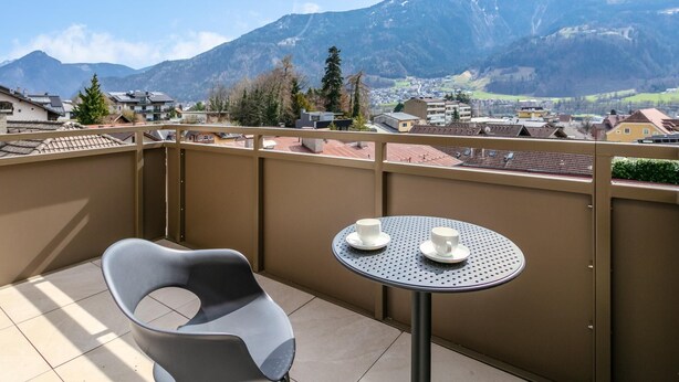 Un balcón con una silla y una mesa, con vistas a un pueblo y montañas.
