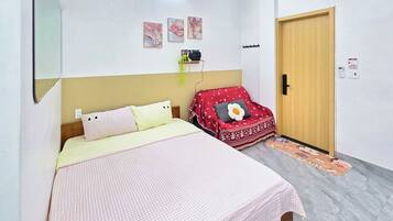 A bedroom with a bed, a red sofa, a wooden door, and a wall-mounted shelf with a plant.