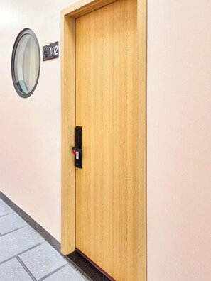 Une porte en bois équipée d’un verrou numérique et d’une plaque indiquant le numéro de chambre : 102.