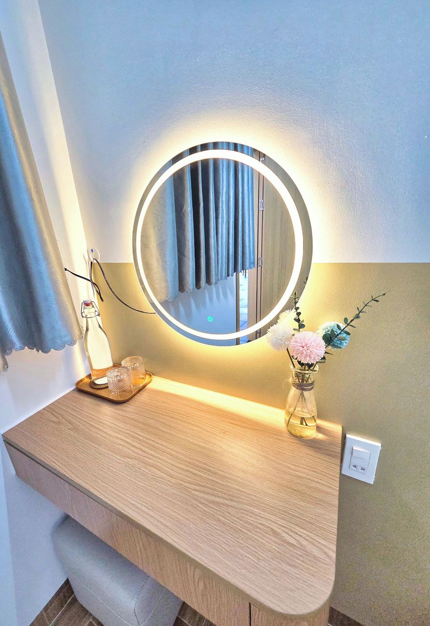 A bathroom vanity with a round mirror, a tray with two glasses, and a vase with flowers.