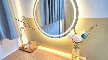 A bathroom vanity with a round mirror, a tray with two glasses, and a vase with flowers.