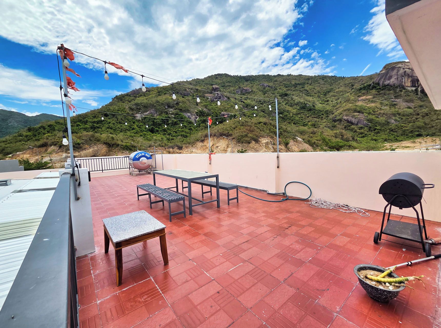 A rooftop terrace with a table and chairs, a barbecue grill, and a hose.