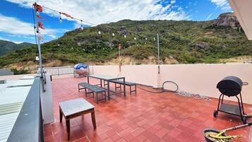 A rooftop terrace with a table and chairs, a barbecue grill, and a hose.