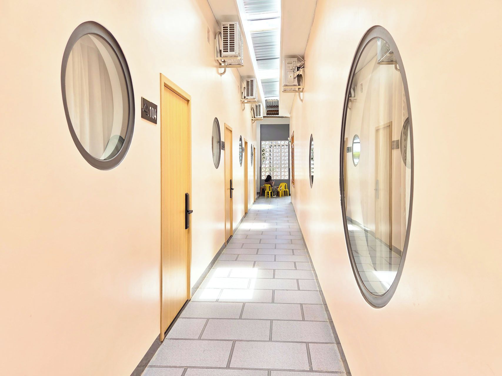 Un couloir d’hôtel avec des miroirs ronds, des portes et un sol carrelé.
