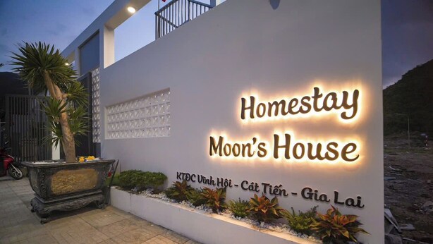 Segnaletica per Homestay Moon's House, dal design moderno, con un vaso decorativo e un ingresso lastricato.