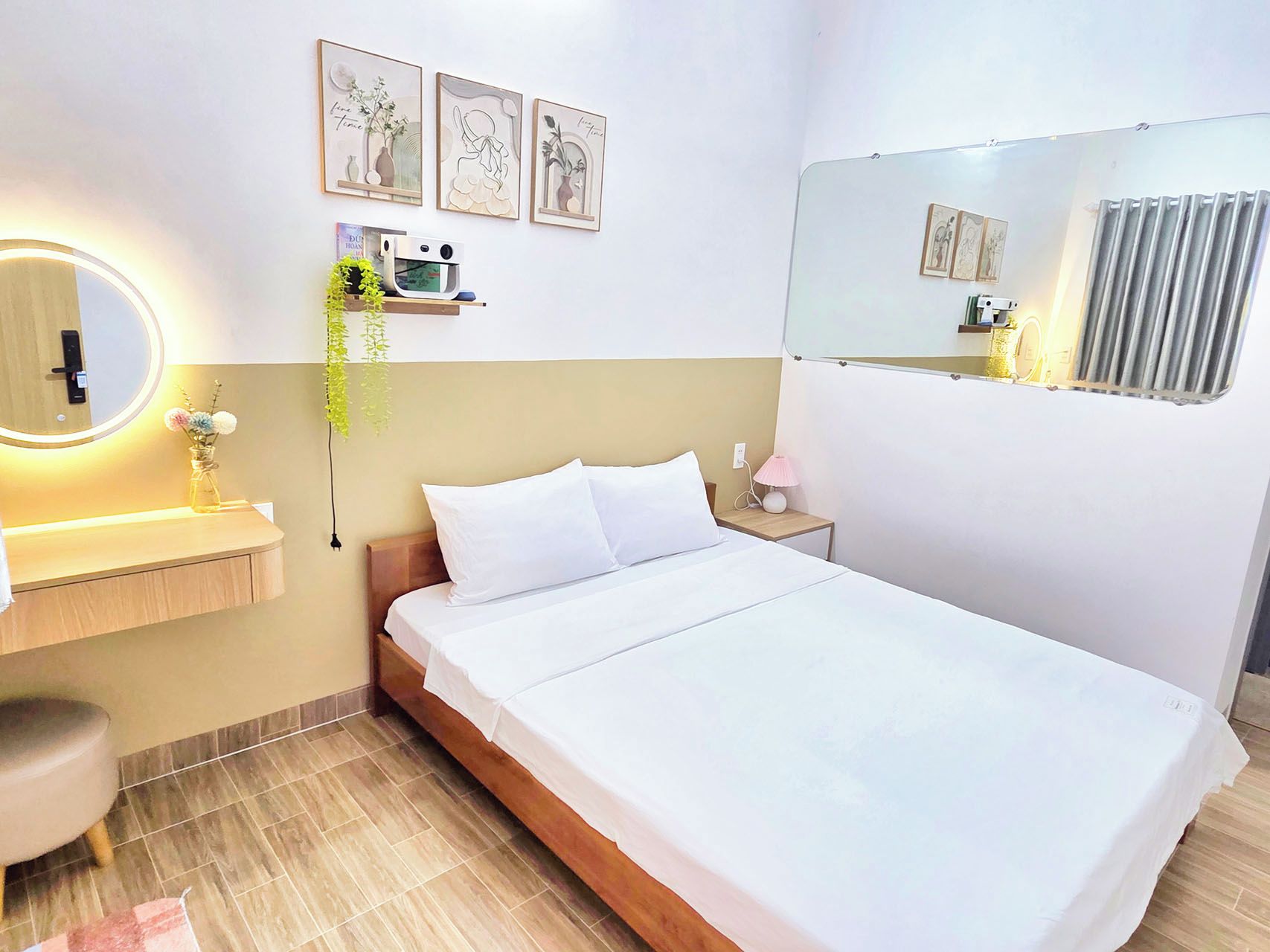 A hotel room with a bed, bedside table, lamp, mirror, and wall-mounted artwork.