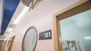 Una camera d'albergo con un grande specchio, una porta con il simbolo del numero e vista su un'altra stanza con finestra e tende.