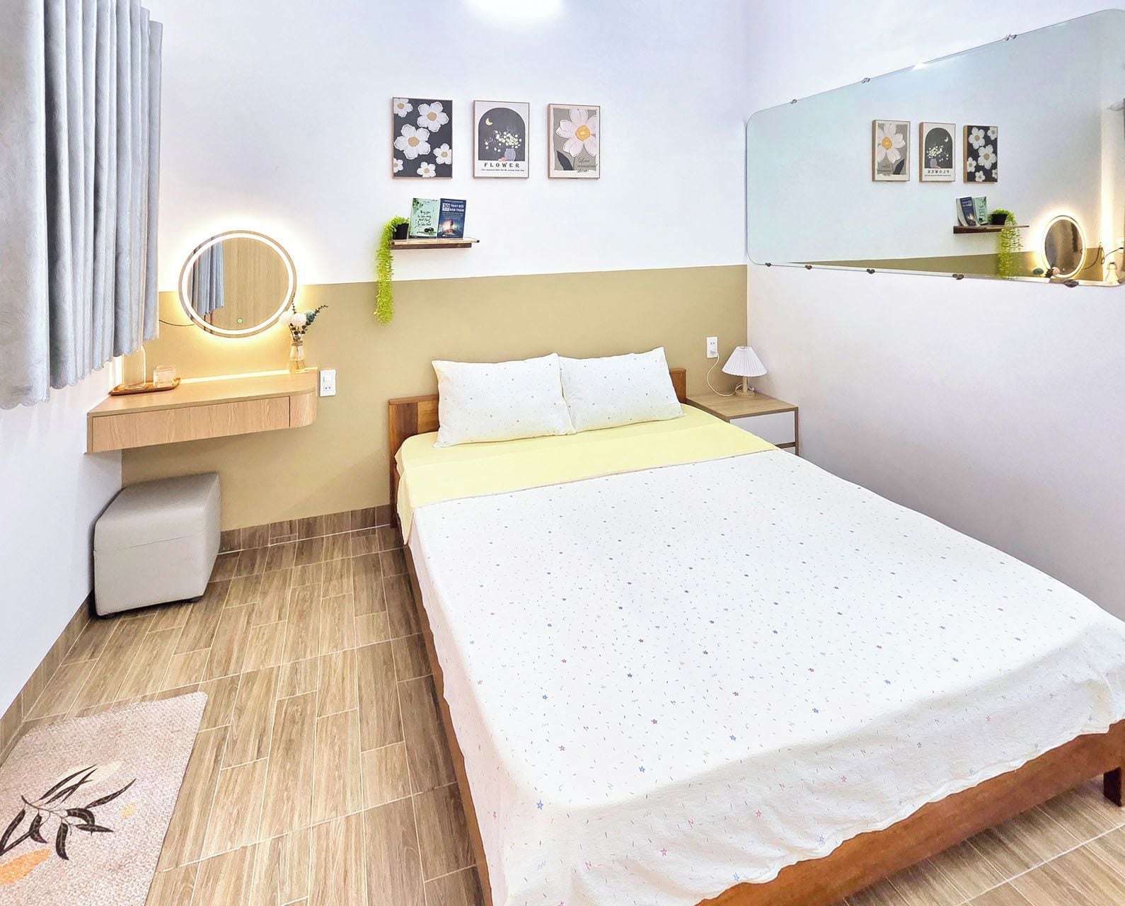 Quarto de hotel com cama, mesa de cabeceira, espelho, arte na parede e uma pequena planta.