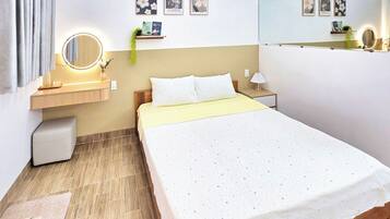 Quarto de hotel com cama, mesa de cabeceira, espelho, arte na parede e uma pequena planta.