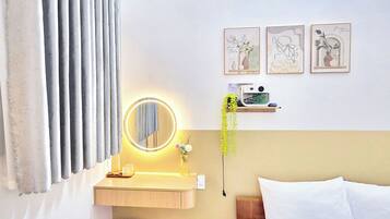 A hotel room with a bed, a bedside table with a lamp, a mirror, and a wall-mounted shelf with decorative items.