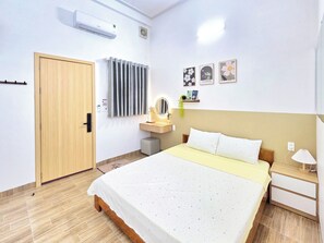 A bedroom with a bed, bedside table, lamp, wall-mounted air conditioner, radiator, and a door.