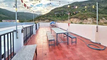 En takterrass med utsikt över ett bergigt landskap, utomhusmöbler och ljusslingor.