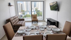 Un salon moderne avec une table à manger pour six personnes, un canapé, un téléviseur et un balcon offrant une vue sur la ville.