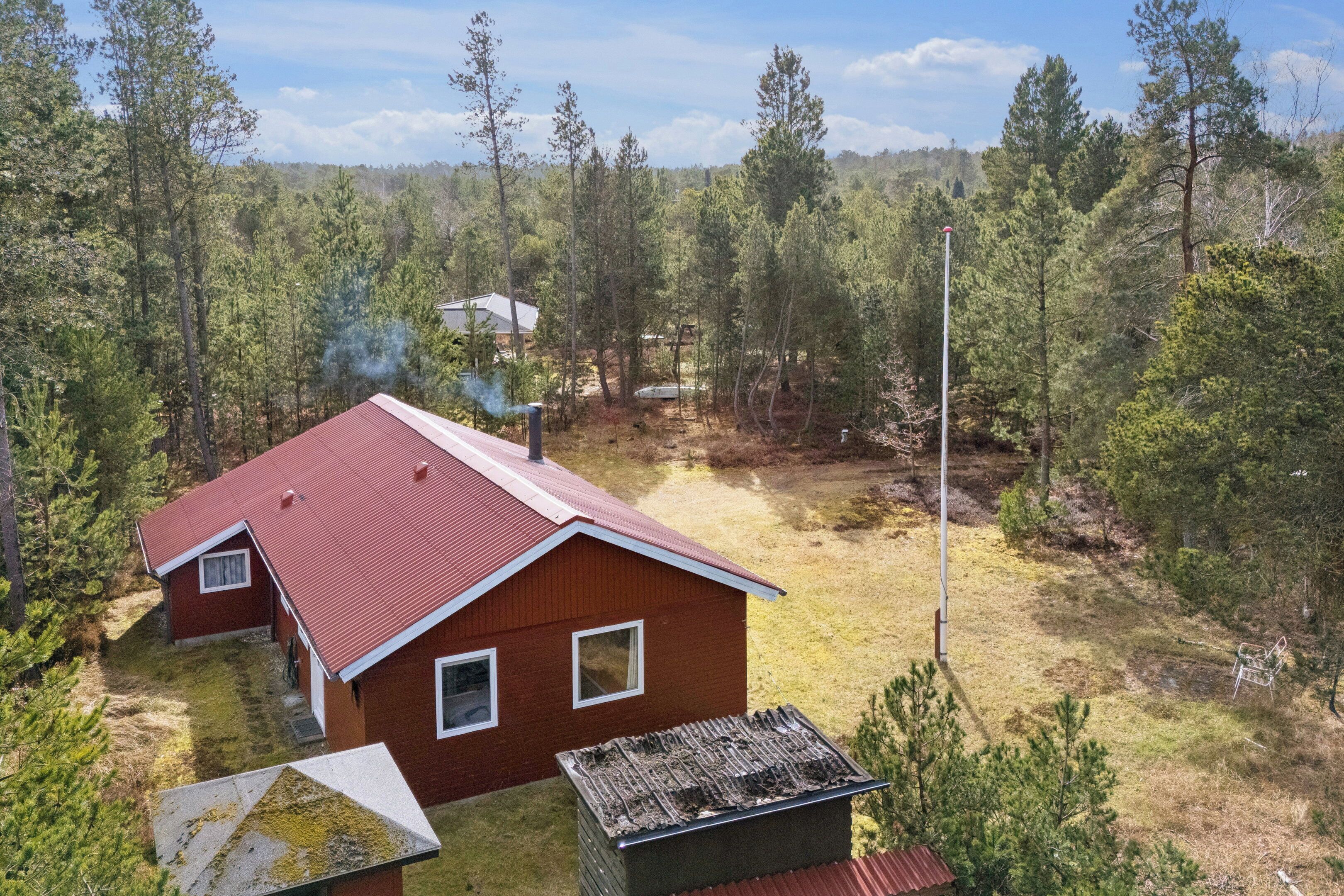 A red house with a metal roof, surrounded by trees and a grassy yard.