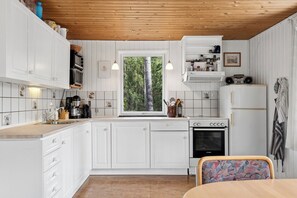A compact kitchen with white cabinets, a window, a Bosch oven, and a refrigerator. - Experience the calm home near sea and forest (Hadsund)