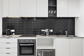 A modern kitchen with white cabinets, a black backsplash, a built-in oven, a dishwasher, and a coffee maker. - City View 1BR | Near Marvel Stadium Dockland (Docklands)