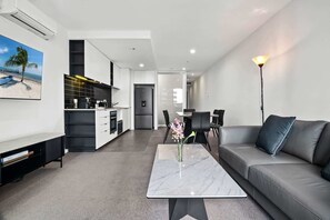 A modern living room with a grey sofa, a marble coffee table, and a dining area with a table and chairs. - City View 1BR | Near Marvel Stadium Dockland (Docklands)