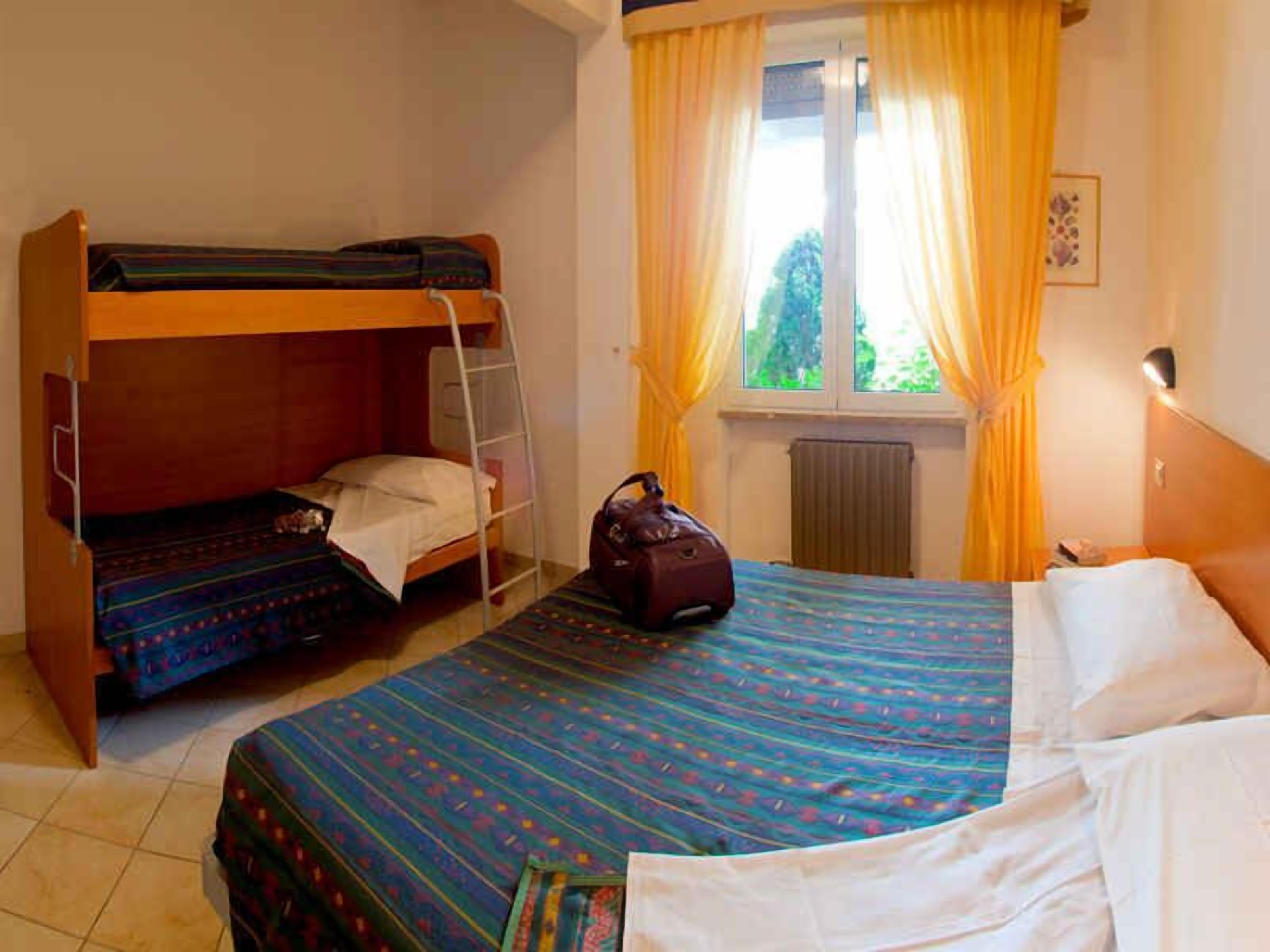 A room with two bunk beds, a single bed, a suitcase, and a window with curtains.