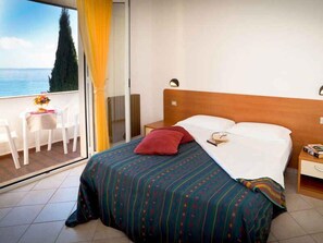 A hotel room with a bed, a bedside table, a chair, and a view of the sea. - Holiday apartment with pool and air conditioning (Pietra Ligure)