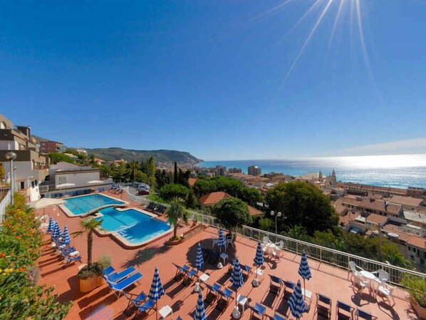 A rooftop pool with lounge chairs and umbrellas, overlooking a coastal cityscape. - Holiday apartment with pool and air conditioning (Pietra Ligure)