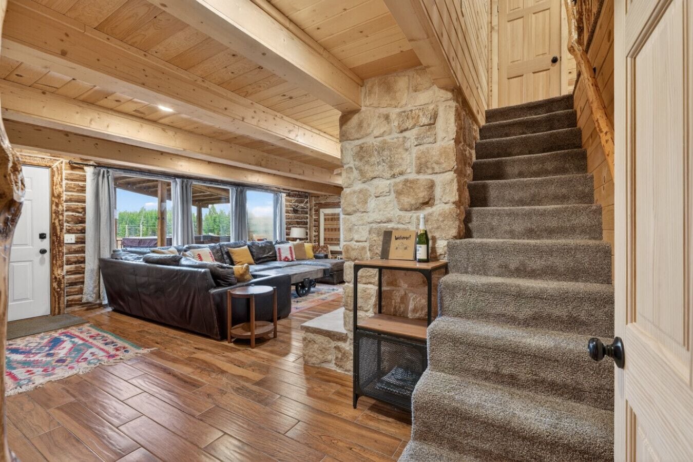 A log cabin interior with a stone wall, wooden staircase, and a sofa set.