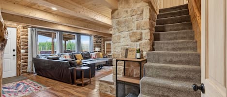 L’intérieur d’une cabane en rondins, avec un mur en pierre, un escalier en bois et un ensemble de canapés.