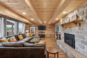 Ein Blockhaus-Interieur mit Kamin aus Stein, einem Ledersofa und einem Fernseher.