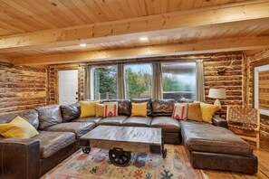 Ein Holzblockhaus-Interieur mit einem großen Ledersofa, einem Holztisch und einem gemusterten Teppich.