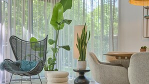 A modern living room with a wicker chair, a round ottoman, and a dining table with chairs.