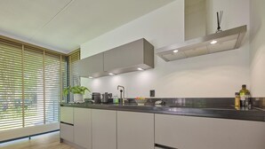 A modern kitchen with a wooden floor, a built-in oven, a sink, and a window with blinds.
