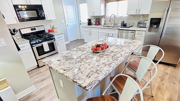 A modern kitchen with white cabinets, a granite countertop, a stainless steel refrigerator, and a central island with bar stools. - Nice Modern Vintage House near Sky Harbor Airport (Phoenix)