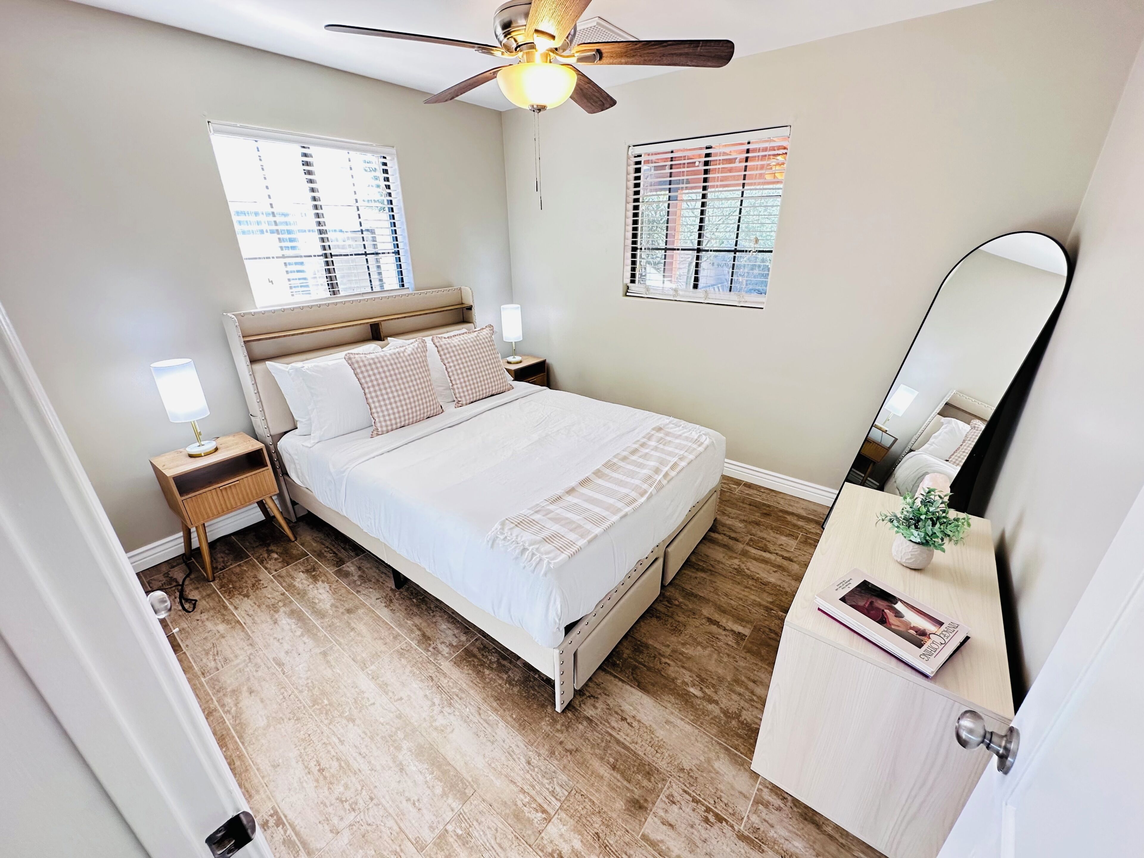 Une chambre à coucher comprenant un lit, des tables de chevet, un ventilateur de plafond et un miroir.