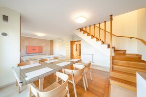 Una sala moderna con comedor, una escalera y un televisor montado en la pared.
