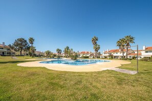 Un área de piscina con varias piscinas, rodeada de césped y palmeras, y edificios al fondo.