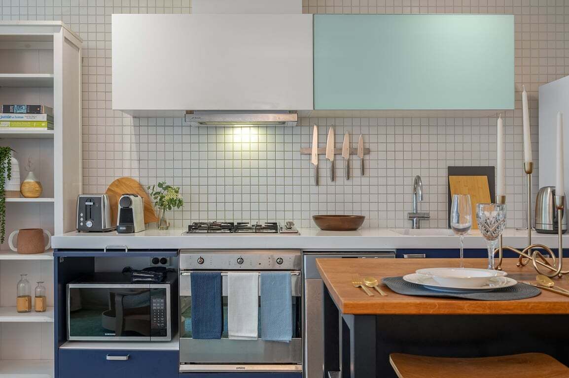A modern kitchen with a microwave, oven, and gas stove. There are knives on the wall, a bowl on the counter, and a wine glass.