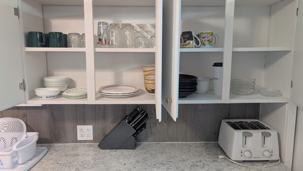 A kitchen with white cabinets, a toaster, a blender, and various dishes and utensils.