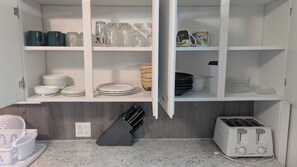 A kitchen with white cabinets, a toaster, a blender, and various dishes and utensils. - Warm & Inviting 2 Bedroom Stay (Timmins)