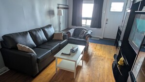 A living room with a black leather sofa, a white coffee table, a television, and a fireplace.
