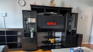 A living room with a black entertainment unit, a television displaying 'NETFLIX,' and a clock on the wall.