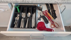 A drawer with utensils, a red cup, and a green grater.