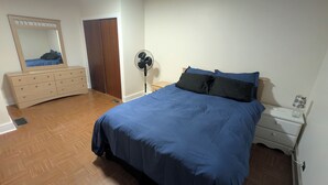 A bedroom with a bed, dresser, mirror, fan, and nightstand.
