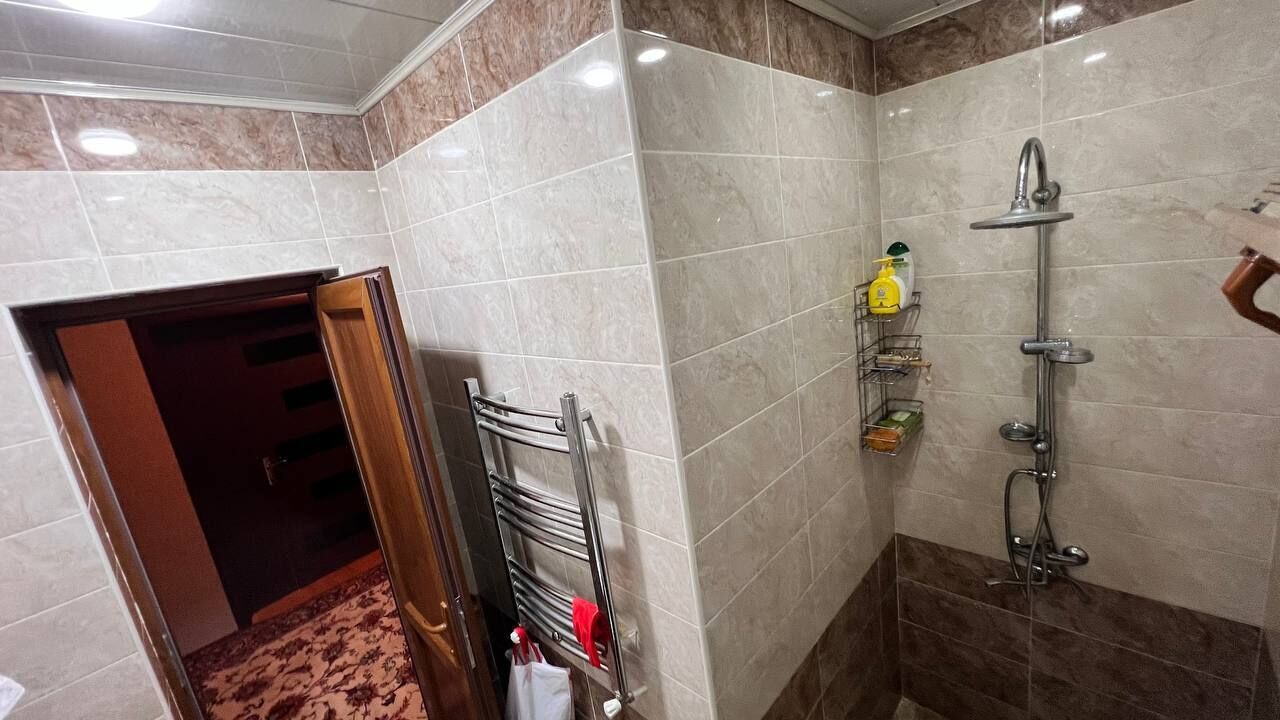 Un baño con ducha, perchero y repisa con artículos de aseo.