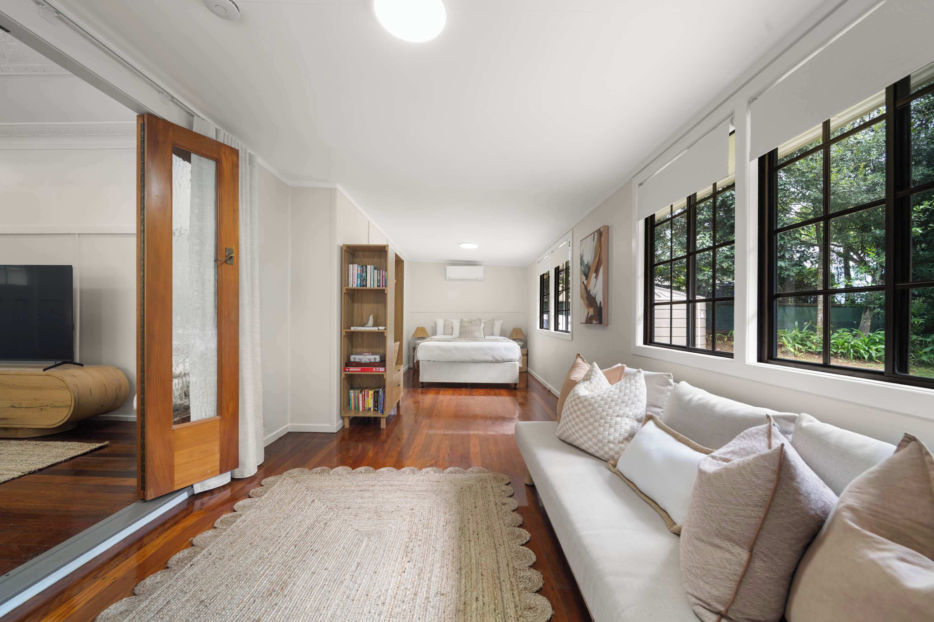 A spacious living room with a sofa, a bookshelf, and a large window with a view of greenery.