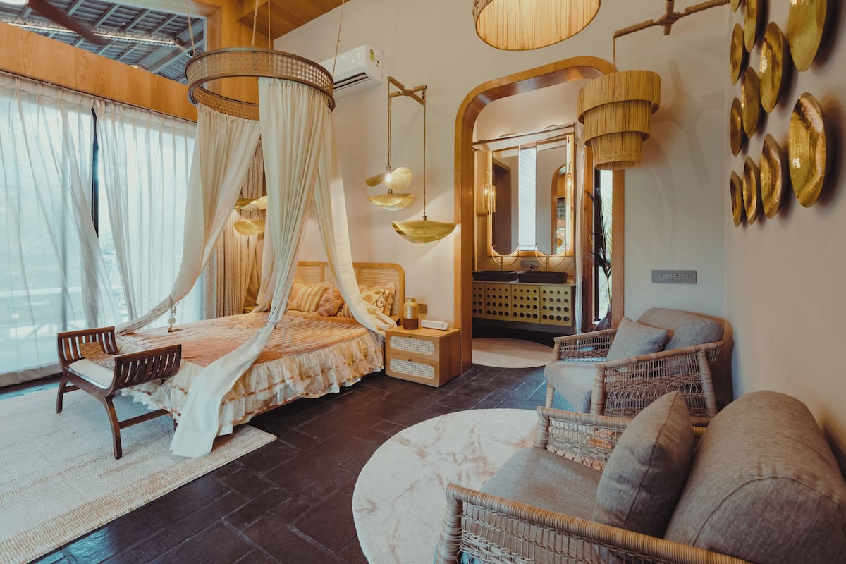 Een slaapkamer met een hemelbed, een zithoek met rieten meubels en een grote spiegel.