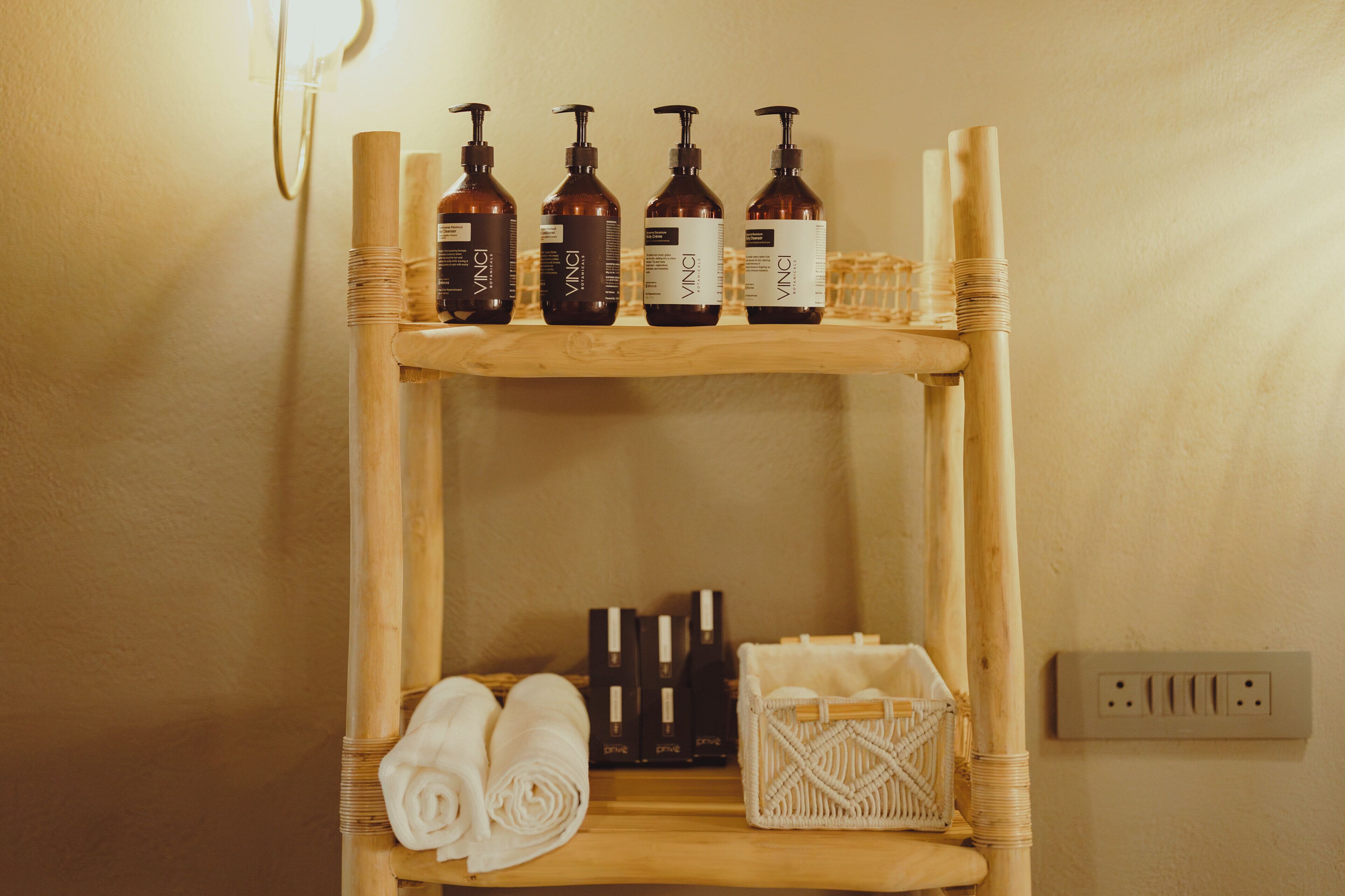 A wooden shelf with bottles and towels, a woven basket, and a wall socket.