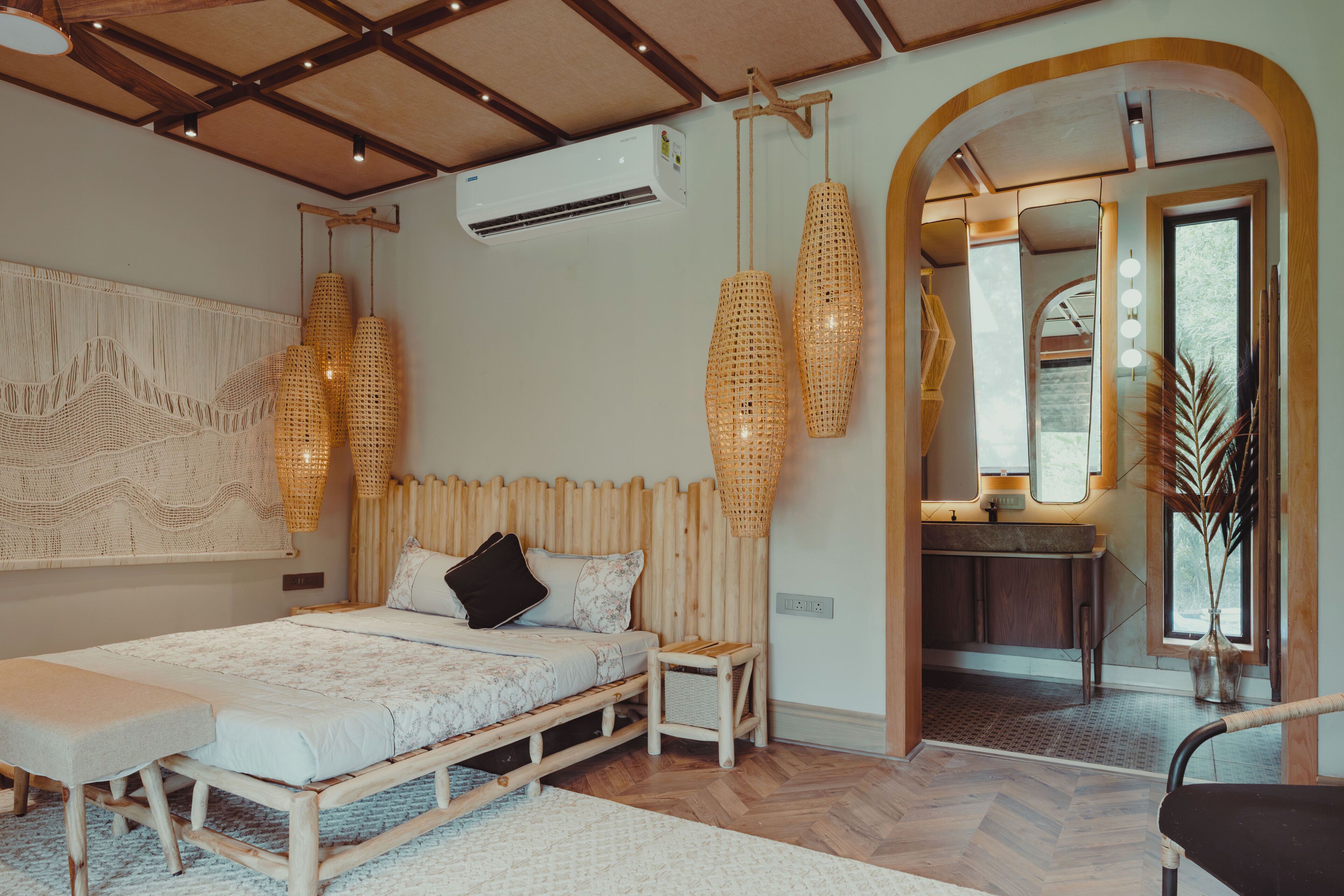 Ein Schlafzimmer mit Bett, Nachttischen, einer Hängeleuchte, einer Klimaanlage und einem durch einen Bogen sichtbaren Badezimmer.