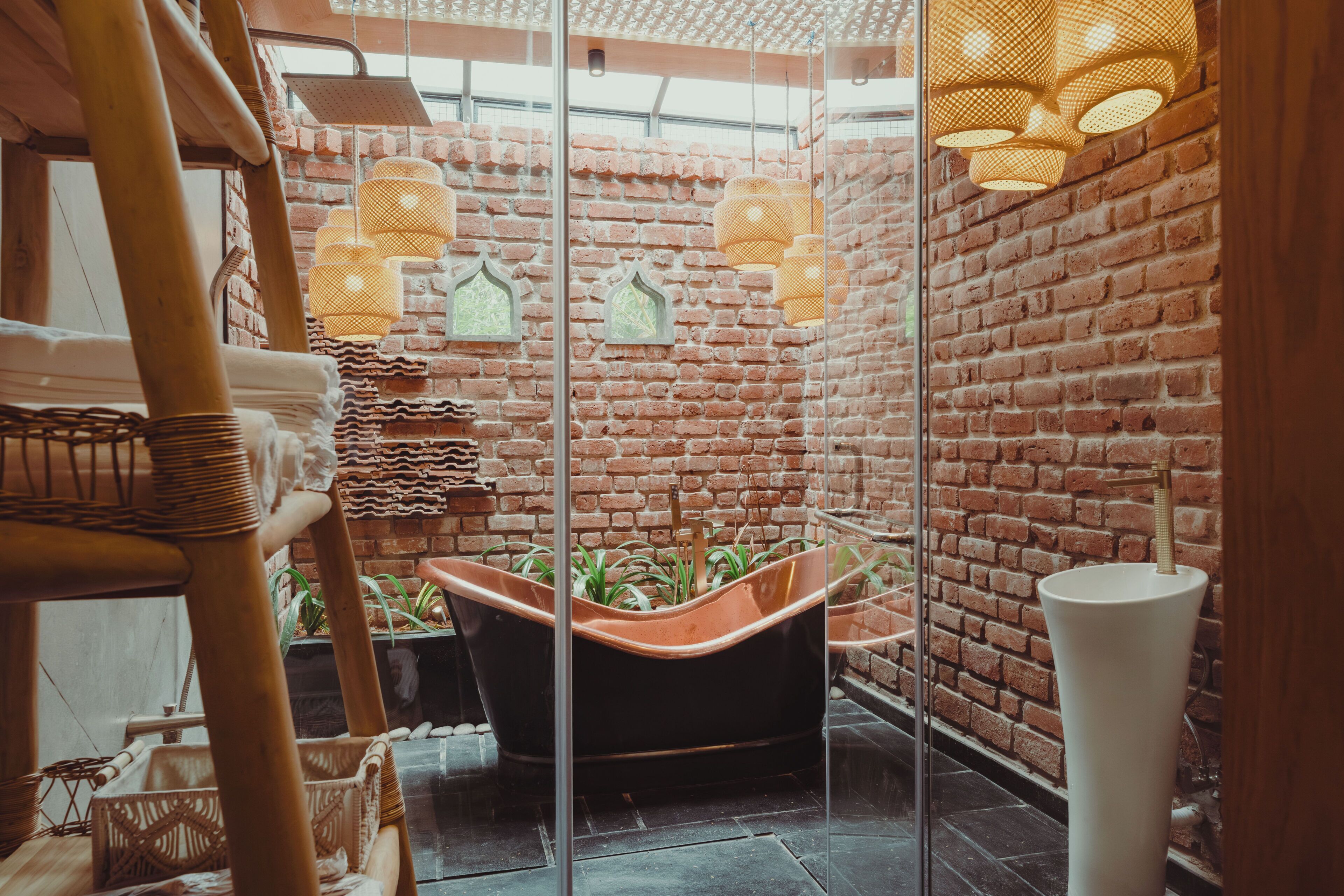 A room with a brick wall, a black bathtub, wicker furniture, and hanging lights.