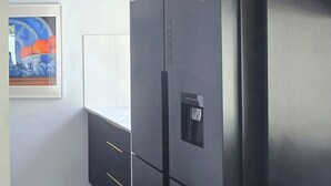 Een moderne keuken met een grote zwarte koelkast, donkere kastjes en een houten vloer.