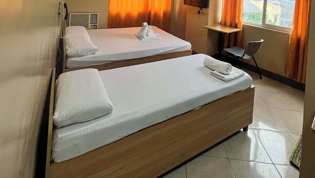 Een hotelkamer met twee bedden, een bureau, een stoel, een raam met gordijnen en uitzicht op de stad.