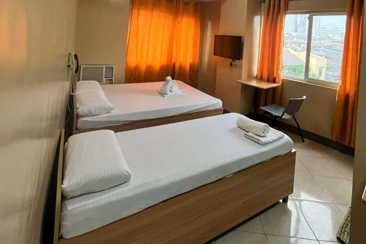 Ein Hotelzimmer mit zwei Betten, einem Schreibtisch, einem Sessel, einem Fernseher und einem Fenster mit Vorhängen.